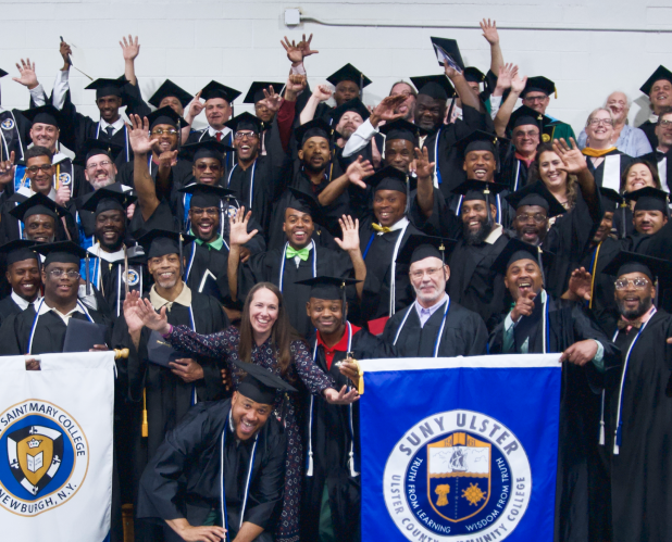 Photo of graduates of Hudson Link for Higher Education in Prison program holding flags for Mount Saint Mary College and SUNY Ulster.