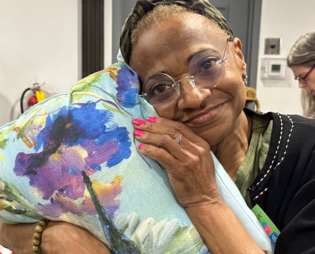 Photo of a Woman smiling and holding a pillow with a floral pattern.