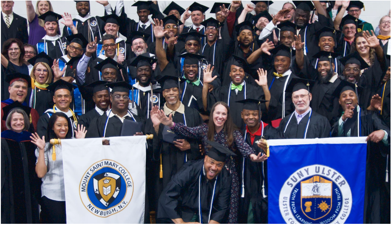 Photo of graduates of Hudson Link for Higher Education in Prison program holding flags for Mount Saint Mary College and SUNY Ulster.