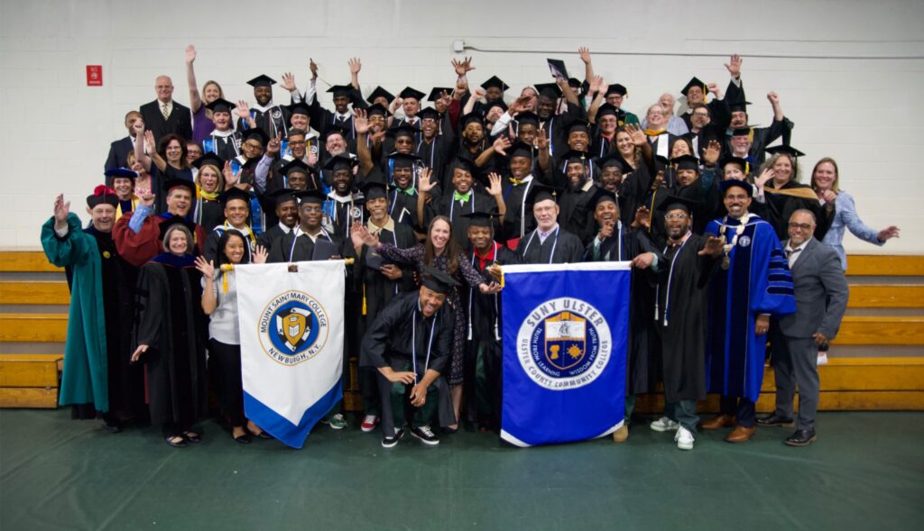 Photo of graduates of Hudson Link for Higher Education in Prison program holding flags for Mount Saint Mary College and SUNY Ulster.